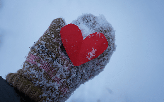 Gloved hand holding a heart in the snow