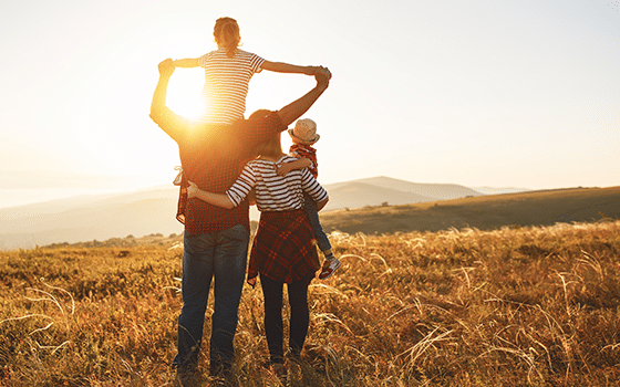 a family with two children looking away from the camera towards the sun in a field