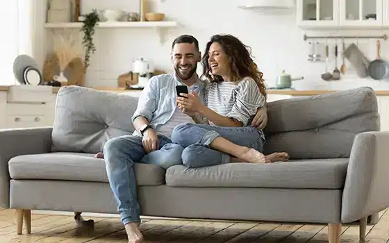 couple sitting on their sofa watching something on their mobile phone