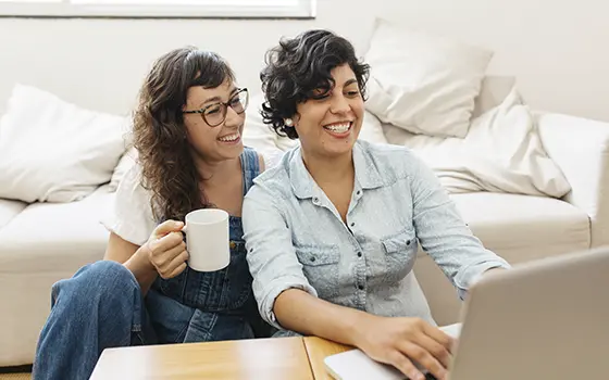 a happy same sex couple smiling while looking at their laptop