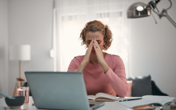 someone with their head in their hands while sat at a desk at home with a laptop