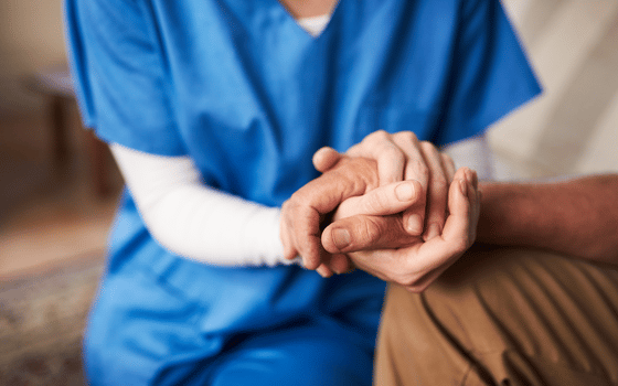 A man and a woman in nurse uniform holding hands with a caring gesture